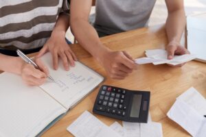 Two people reviewing financial documents and calculating debt consolidation savings at a desk