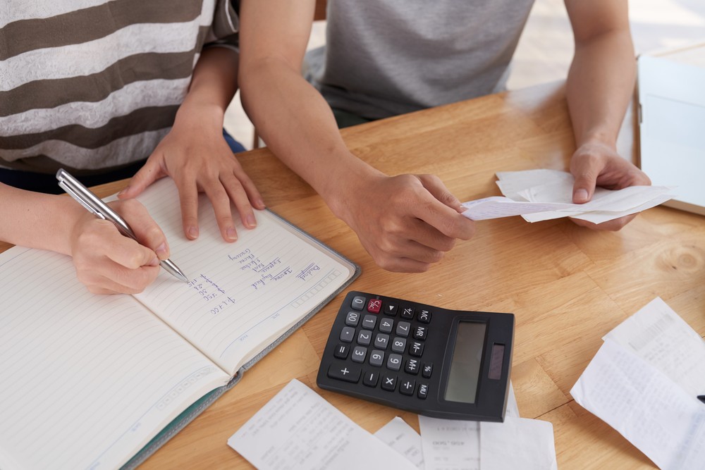 Two people reviewing financial documents and calculating debt consolidation savings at a desk