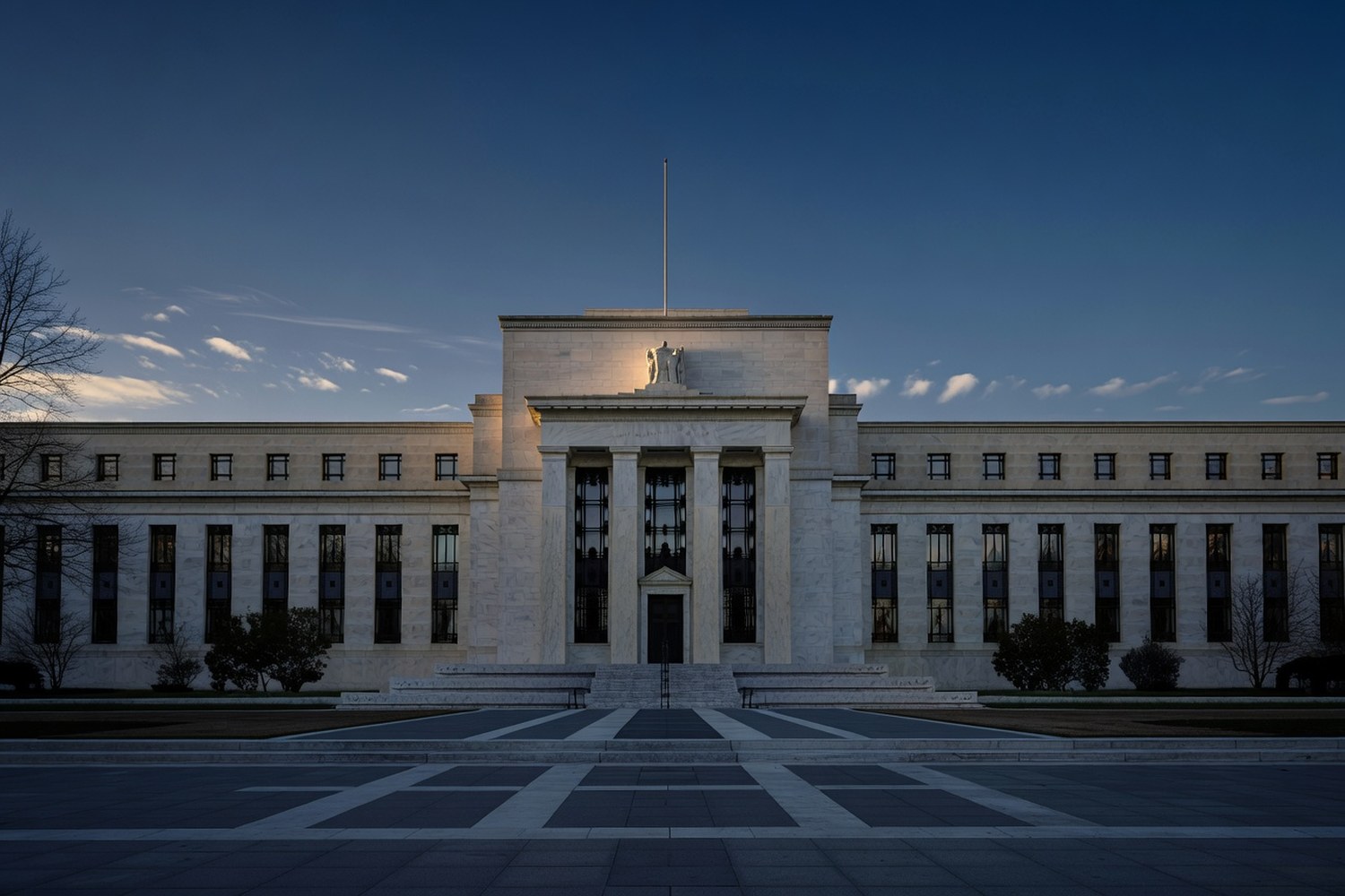 Symmetric front view of the Marriner S. Eccles Federal Reserve Board Building at dawn with warm golden light on the pediment and cool blue pre-sunrise sky