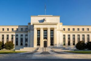 Marriner S Eccles Federal Reserve Board building exterior in Washington DC photographed in late golden hour light with white marble facade central pedimented portico Doric columns broad symmetrical wings and wide stone steps against a deep blue afternoon sky