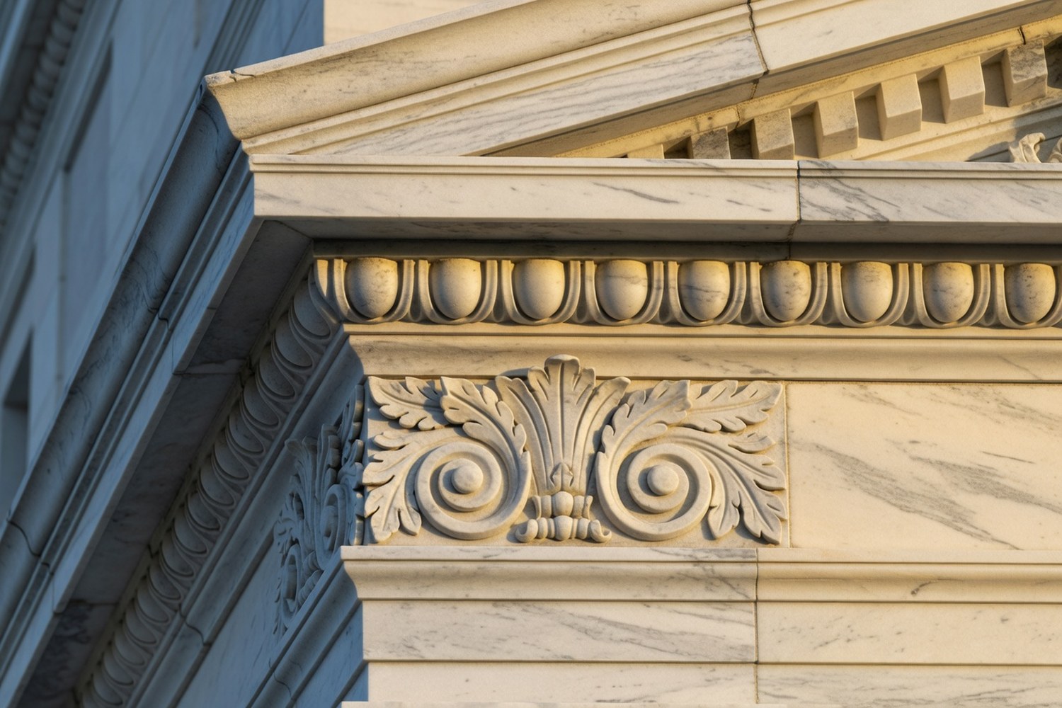 Macro architectural detail of classical stonework on a major institutional building exterior showing carved egg and dart molding with dentil row and central acanthus leaf scrollwork carving in warm late afternoon side light against deep cool shadows