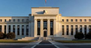 Wide cinematic photograph of the Marriner S Eccles Federal Reserve building in Washington DC at golden hour with dramatic side lighting on the white marble neoclassical facade tall fluted columns casting long shadows the eagle and seal above the central pediment an American flag at the entrance and a dignified institutional mood
