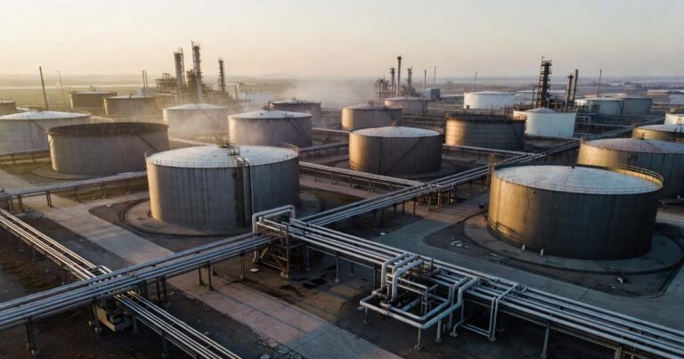 Aerial view of a large industrial oil refinery with fuel storage tanks and pipelines at golden hour under a hazy sky