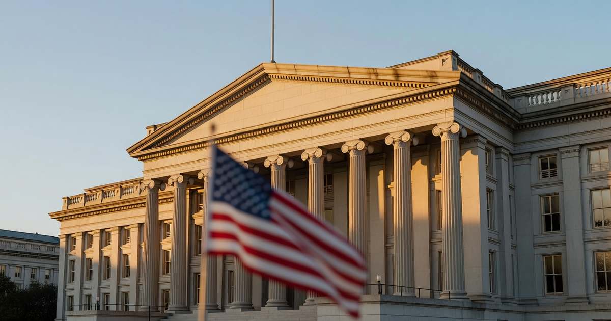 The United States Treasury building neoclassical stone facade with tall columns in Washington photographed at golden hour with a softly blurred American flag in the foreground under a clear sky