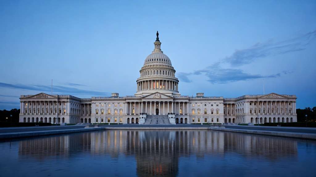 The United States Capitol dome illuminated at dusk viewed across the calm surface of a reflecting pool under a cool blue evening sky with soft clouds