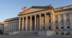The neoclassical stone facade of the United States Treasury Department building in Washington photographed in golden late afternoon light with an American flag flying on a pole against a clear sky