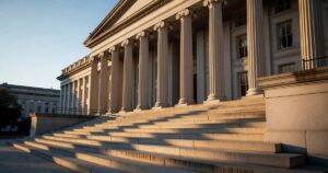 The neoclassical stone facade and columned portico of the United States Treasury Department building in Washington DC, photographed from the base of its wide granite steps in late afternoon golden light.