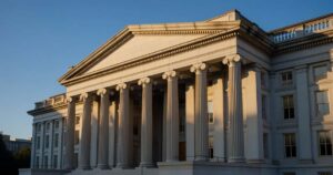 The columned neoclassical facade of the United States Treasury Department building in Washington lit by warm late afternoon sun against a deep blue sky