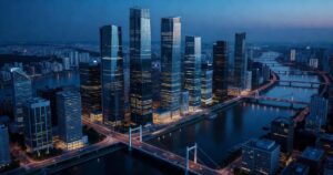 Aerial view of a modern financial district photographed at blue hour, glass office towers lit from within above a wide river and lit bridges, cool blue sky over warm amber window light