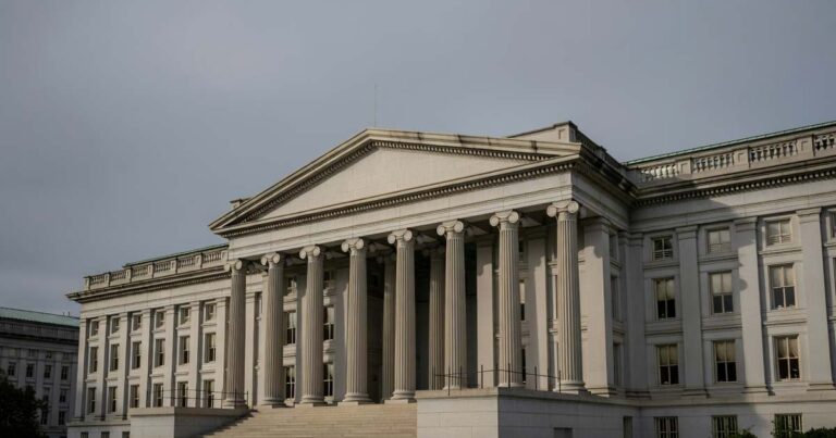 The columned stone facade of the United States Treasury building in late afternoon light beneath an overcast gray sky