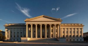 The neoclassical limestone facade and columned portico of the United States Treasury building in Washington D.C., lit by low golden hour sunlight under a deep blue sky