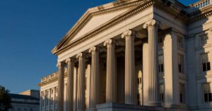 Late summer sunlight rakes across the limestone columns of the United States Treasury Building in Washington DC under a deep blue sky