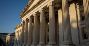 Sunlit limestone columns along the front facade of the United States Treasury building in Washington DC under a clear deep blue afternoon sky