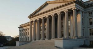 The neoclassical stone facade and Ionic columns of the United States Treasury Department building in Washington DC, lit by low golden morning sunlight, with empty granite steps in the foreground and a clear pale sky above