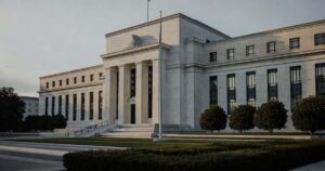 The neoclassical limestone facade of the Federal Reserve Marriner S. Eccles Building in Washington photographed at early morning with tall fluted columns deep window recesses raking dawn light across the stone long cool shadows falling on the empty plaza a bare flagpole and low trimmed hedges in the foreground beneath a pale overcast sky