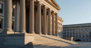 Dawn light rakes across the limestone columns of the United States Treasury building in Washington, casting long shadows down the front steps under a clear early autumn sky.