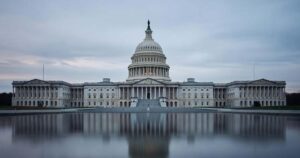 The United States Capitol dome and its west front reflected in the still water of the Capitol Reflecting Pool under a pale overcast sky at dusk.