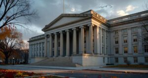 The neoclassical stone columns of the United States Treasury Department building in Washington D.C. photographed at dawn in warm low-angle autumn sunlight, with bare tree branches framing the left edge and an overcast sky breaking into light above the roofline.
