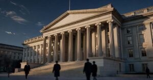 The neoclassical United States Treasury Building in Washington DC photographed at golden hour with warm low sunlight raking across its tall limestone columns and casting long shadows down the front steps, a few blurred pedestrians in dark business coats walking past in the foreground, deep blue autumn sky with thin high clouds above the roofline